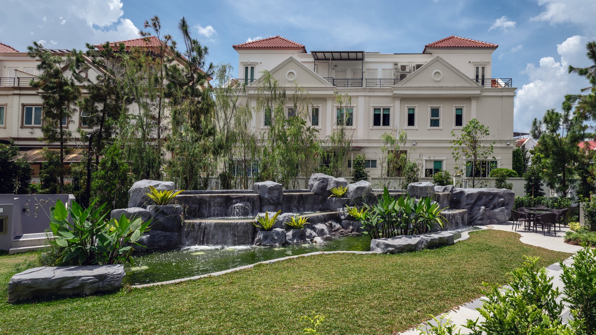 Rock waterfall cascading into a landscaped pond beside a lawn and outdoor dining area at Belgravia Ace